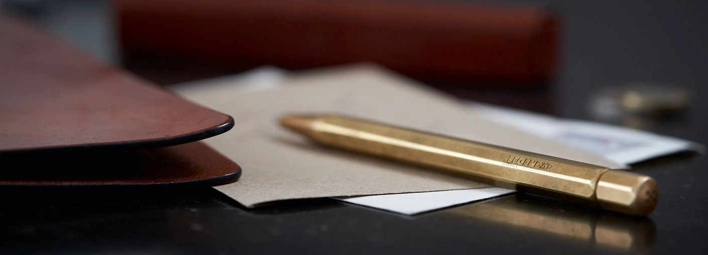 Legendär Kugelschreiber – Messing-Schreibgerät mit Briefumschlägen und Lederaccessoires Legendär Kugelschreiber aus Messing auf Briefumschlägen, daneben ein Lederetui und Dokumentenmappe