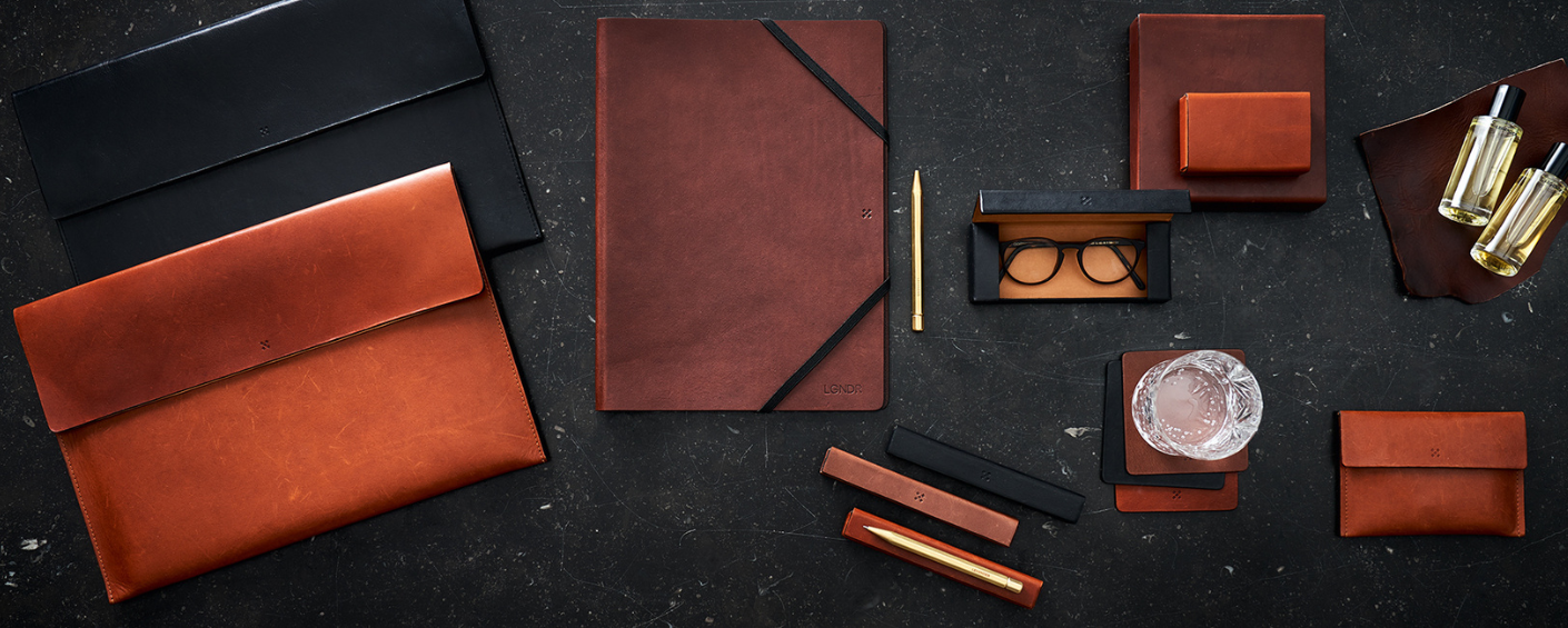 Lederaccessoires und Parfums von Legendär – Briefmappen, Notizbuchhüllen, Etuis und Flakons auf dunklem Hintergrund im Flatlay-Stil